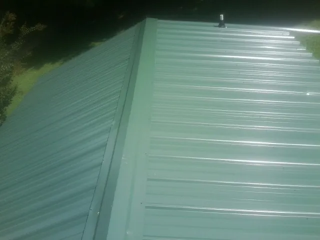 New green metal panels meeting at the ridge of a roof — Flat Roof Repair work by our crew in Cynthiana